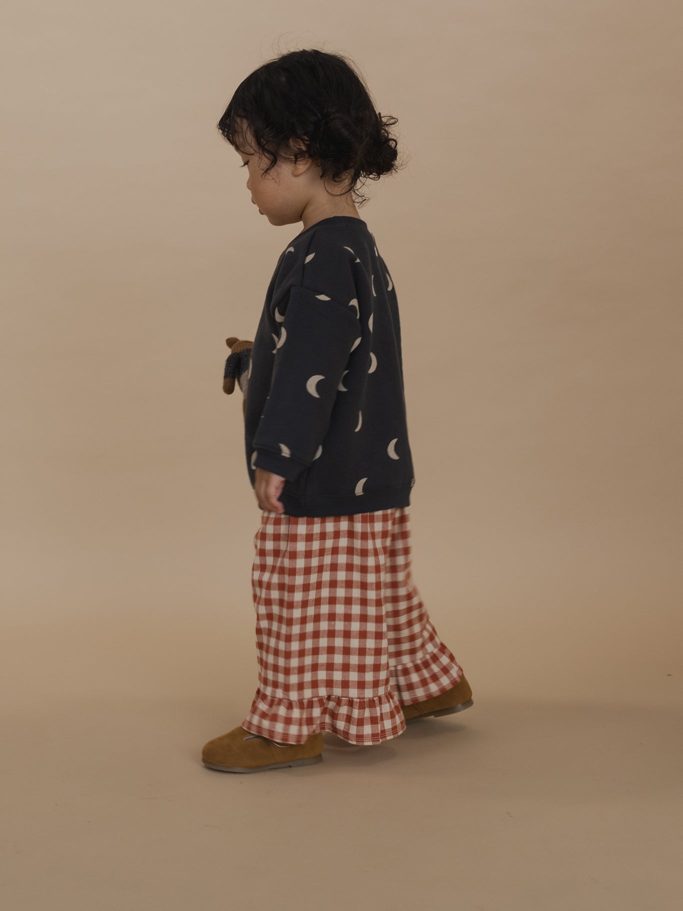 toddler in red and cream gingham culottes with frill hems, and black sweatshirt with cream moon print