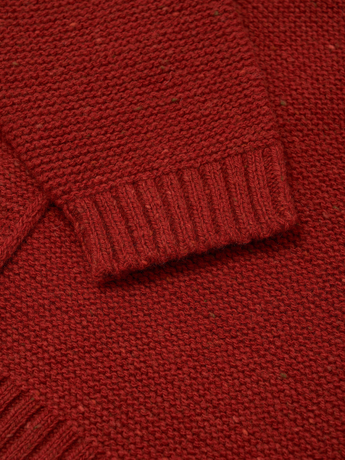 Close-up of a red knit sweater showing the ribbed cuff and textured fabric.