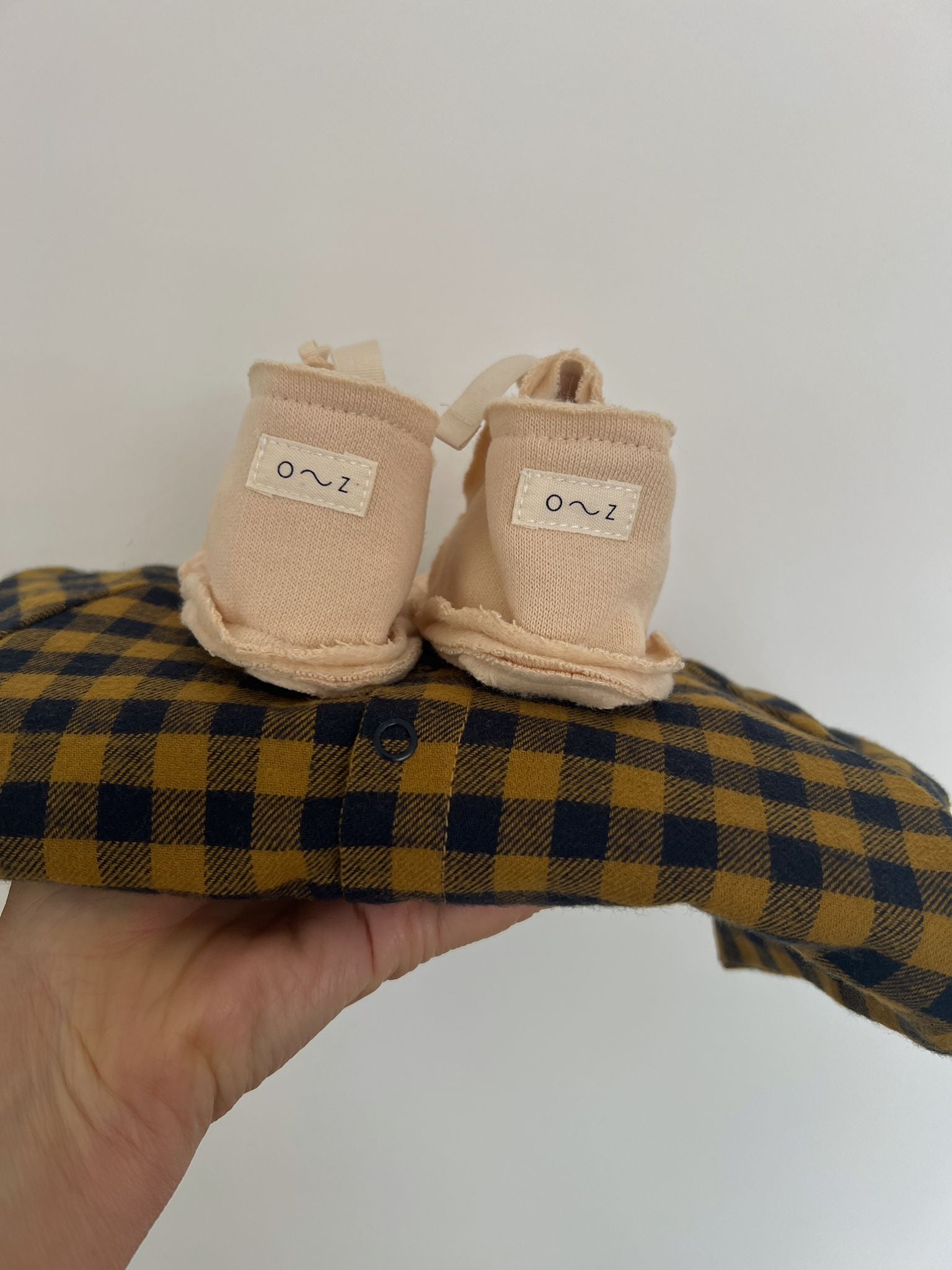 hand holding folded gingham baby onesie with pebble cream terry cotton baby booties on top