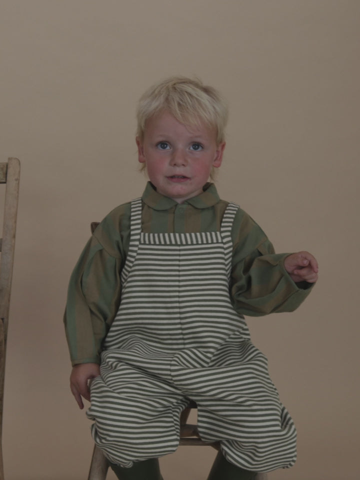 toddler in oversized green and white striped dungarees with lodge shirt and rain boots, stomping feet