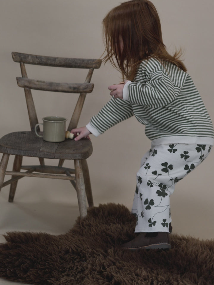 toddler in green and white striped sweatshirt, and pants with clover print, placing items in a cup