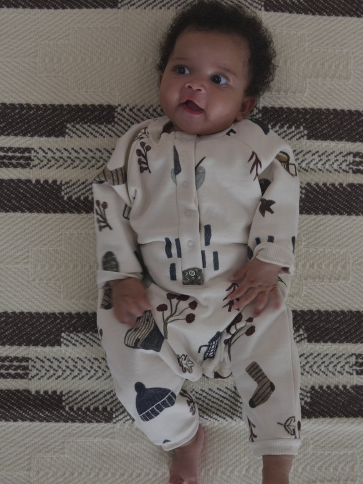 baby in cream undyed cotton onesie with cosy nature-themed hand-drawn prints, waving arms