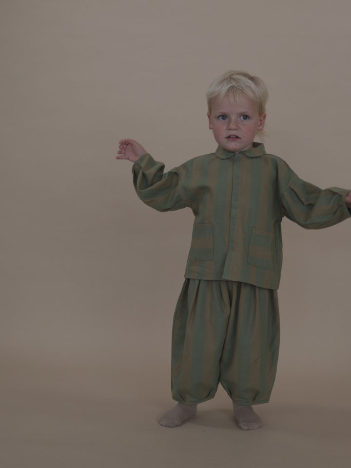 toddler wearing balloon pants in cream and green stripes with matching lodge shirt, waving arms