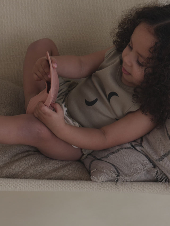 toddler in summer vest with black moon print sitting sideways on chair playing with swimming fins