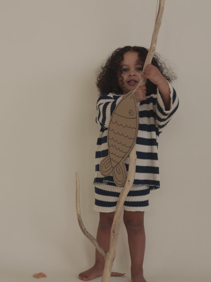 toddler in rib knitted sailor stripes sweater & matching shorts playing with branch & cardboard fish