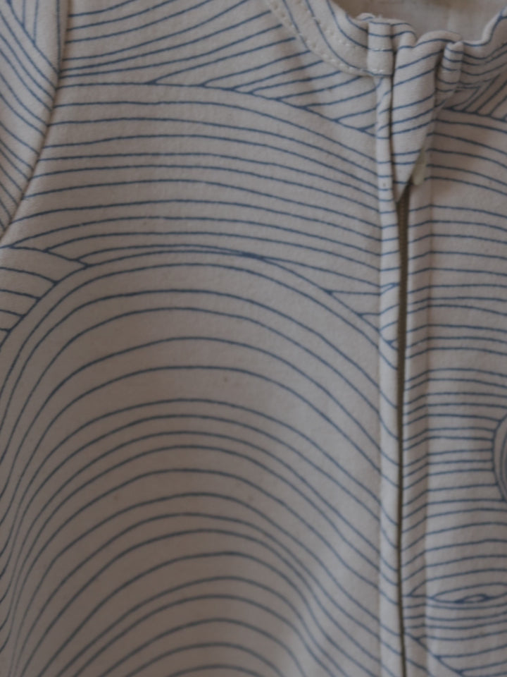 close up of baby cream undyed cotton zip sleepsuit with flowing blue Seascape line-drawn ocean waves