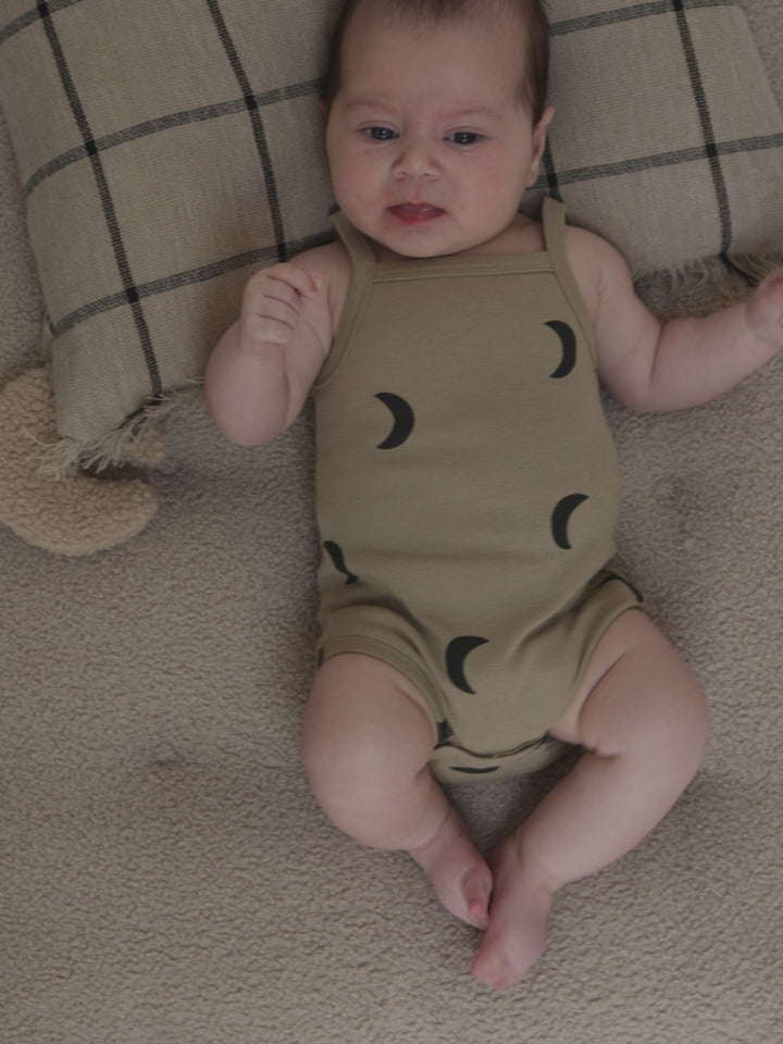 baby in beige tank bodysuit with black moons lying on cushion