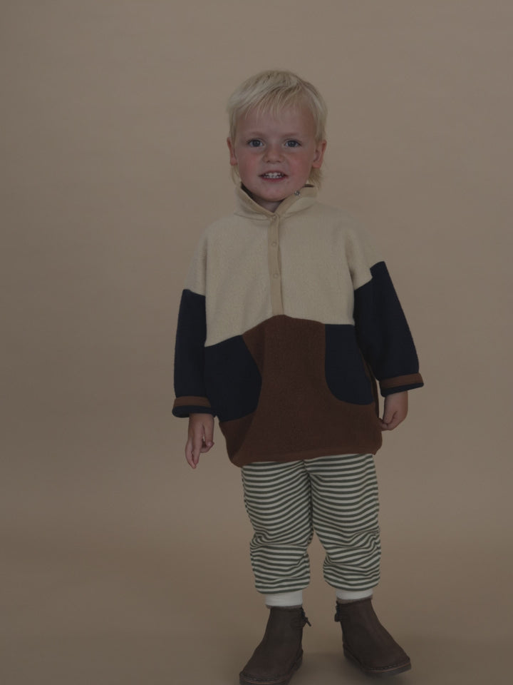 toddler in fern green and white striped sweatpants, and colour block sweater jumping