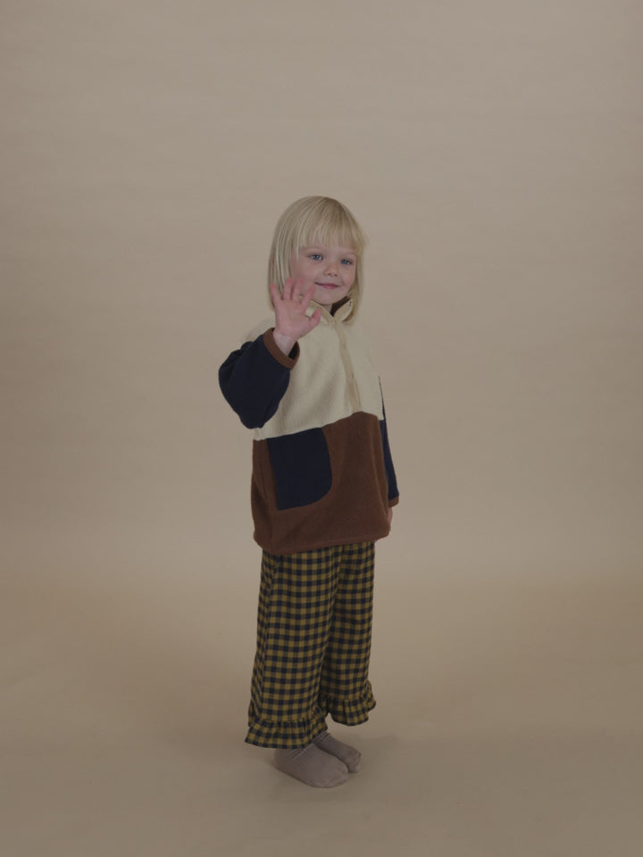 toddler in navy and yellow gingham culottes with frill hems, and colour block sweater waving hand