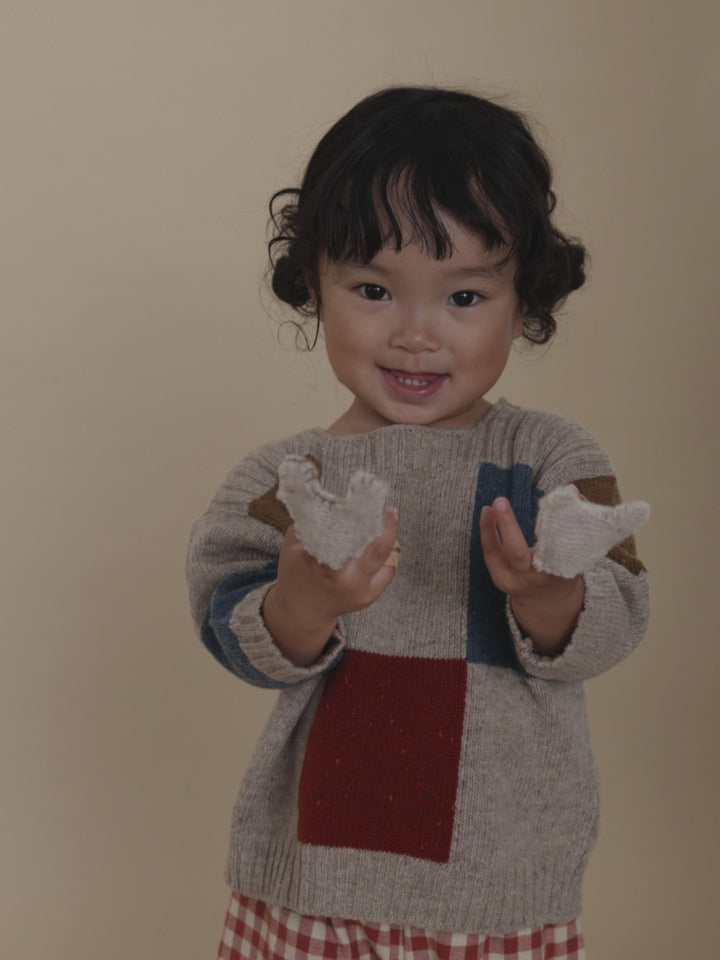 toddler in beige colour-block patchwork wool jumper with square neck, playing with finger puppets