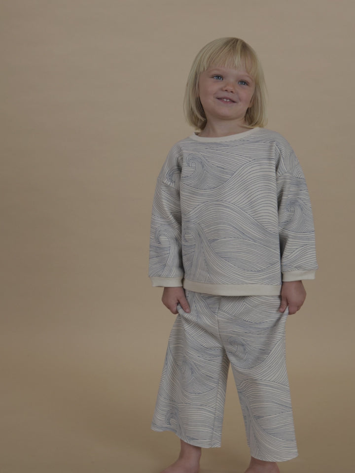 toddler in matching sweatshirt and pants with blue line-drawn ocean waves, twirling and posing