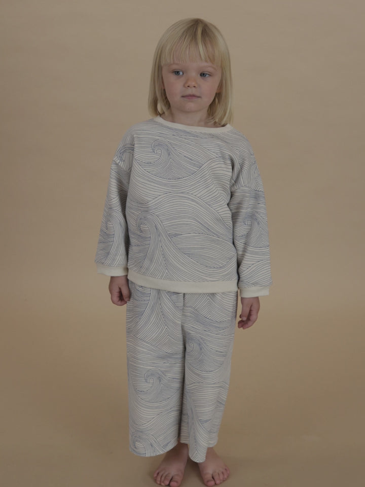 toddler in matching sweatshirt and pants with blue line-drawn ocean waves, jumping