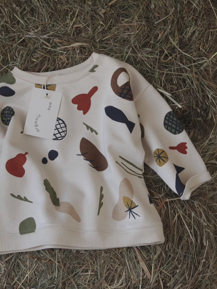 close up video of undyed cotton cream sweatshirt with fruits vegetables & basket prints