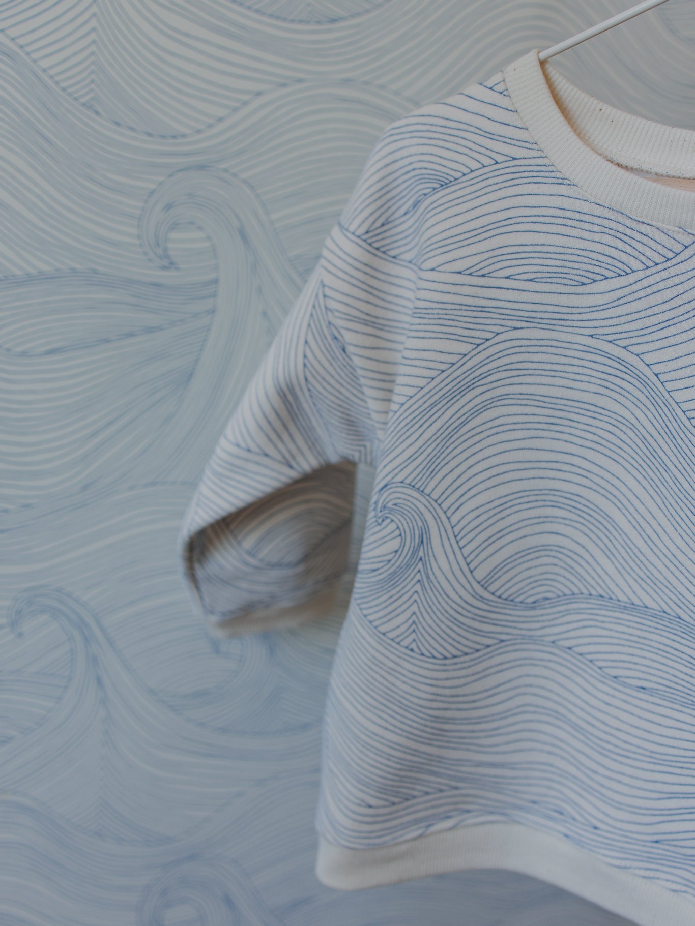 close up of cream sweatshirt with blue line-drawn ocean waves against Seascape ocean waves wallpaper