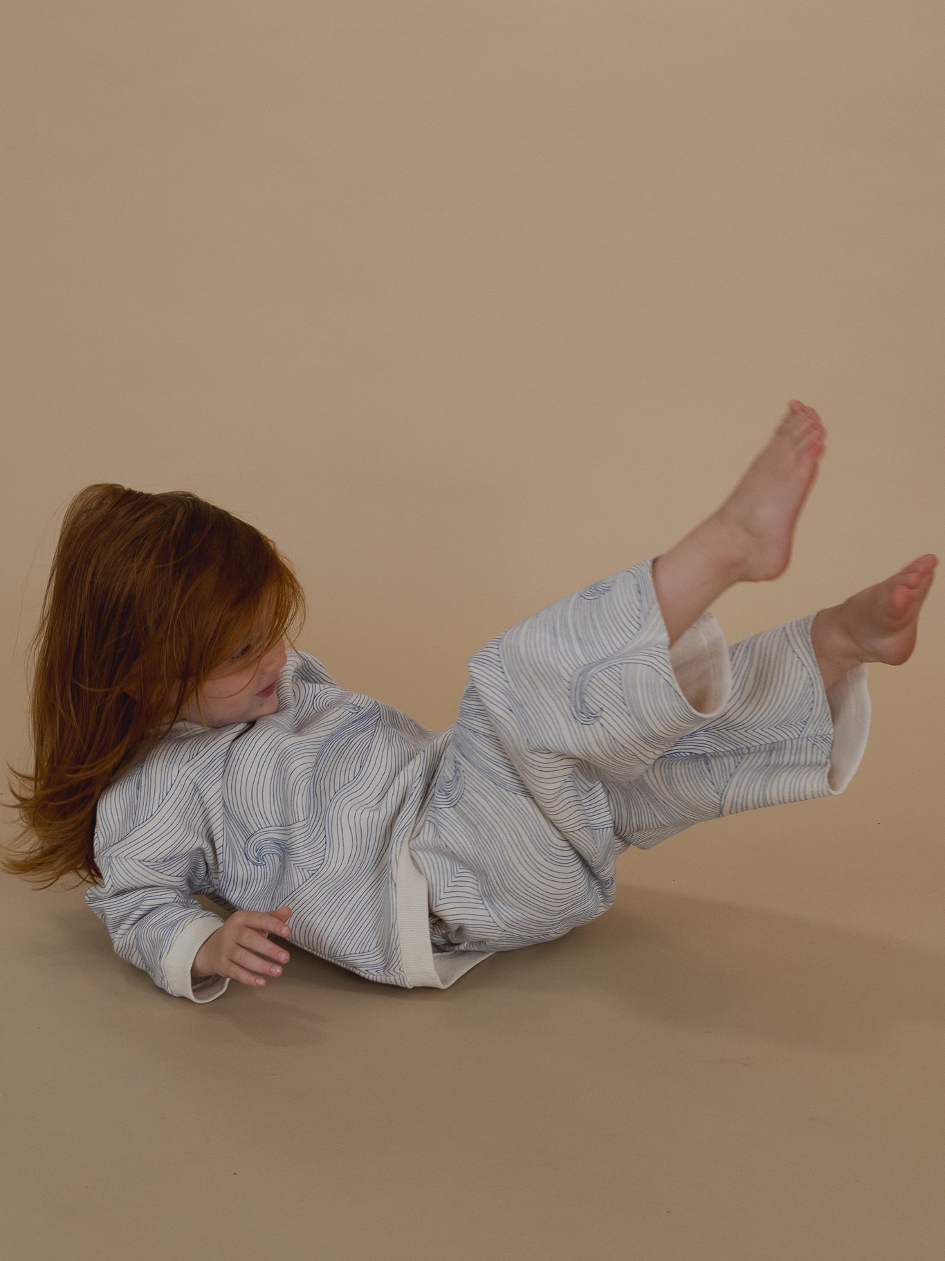 toddler in sweatshirt with blue Seascape line-drawn ocean waves and matching wide leg pants, lying down