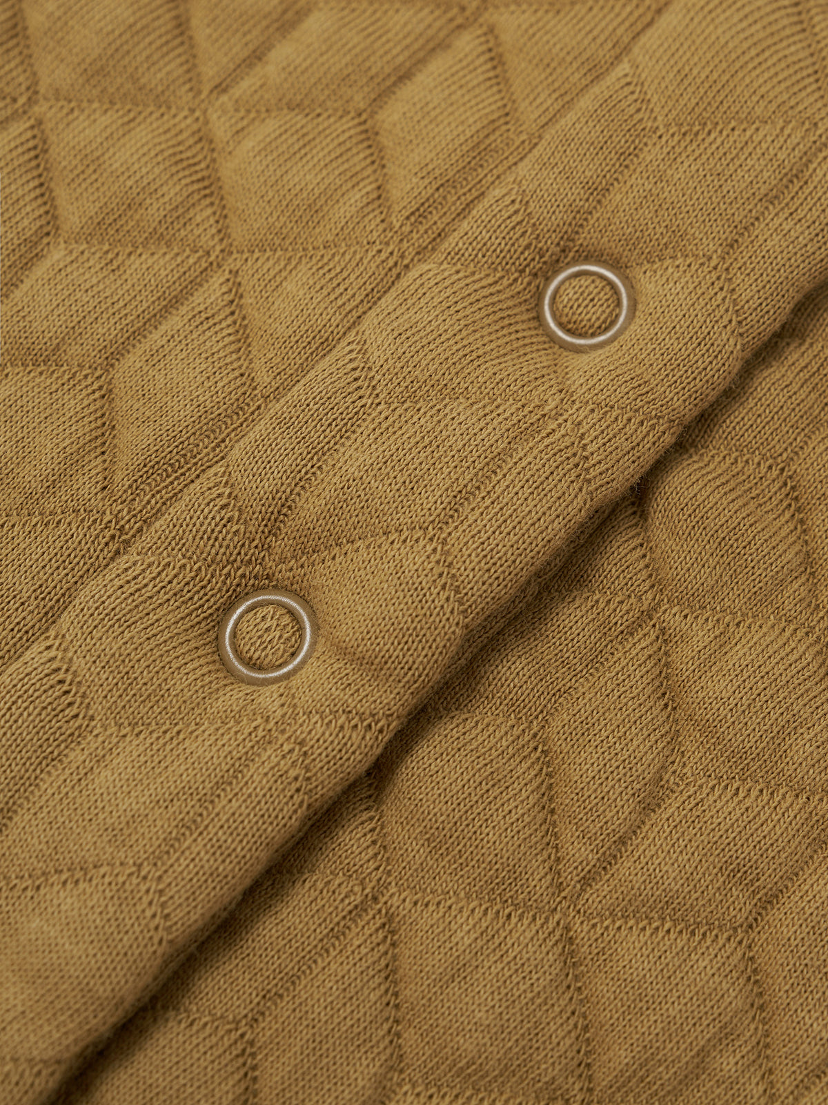 Close-up of a quilted mustard yellow fabric with a diamond pattern and two silver metal grommets.