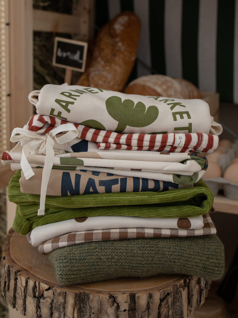 stack of folded baby & toddler clothing with green red brown colours patterns prints on wooden stool