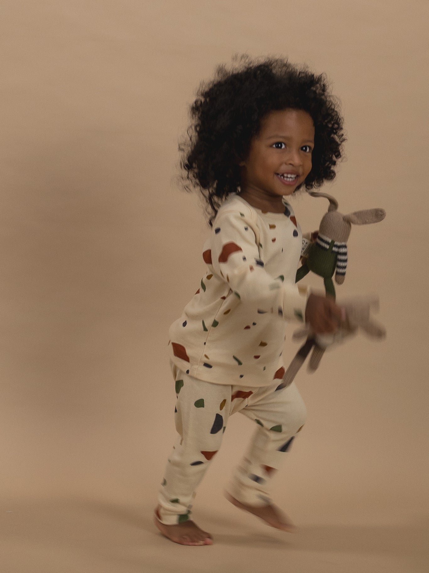 toddler in ribbed cotton long-sleeved top & leggings set with terrazzo print, running with toys