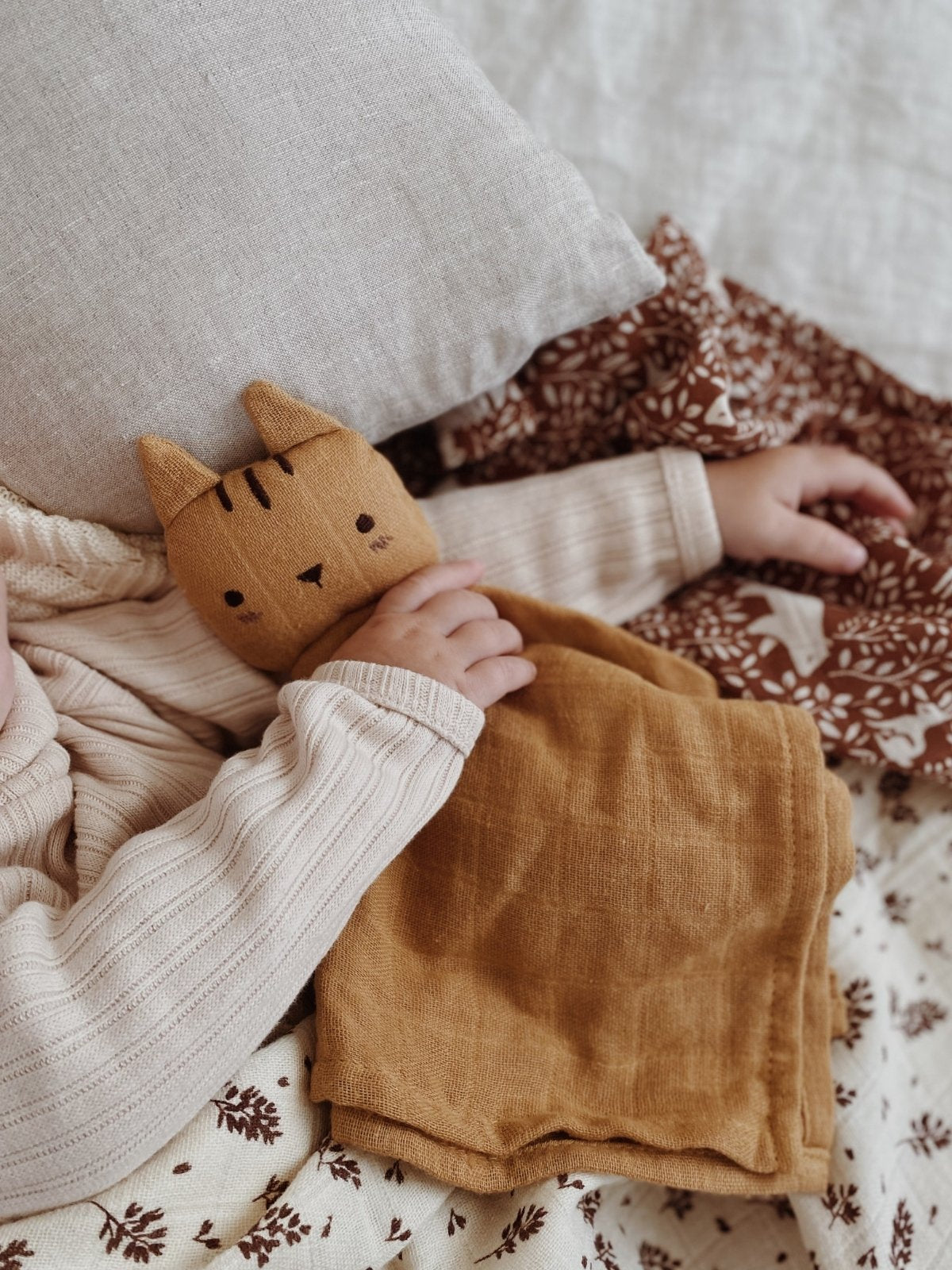 Child holding a brown cat-shaped pillow on a patterned blanket