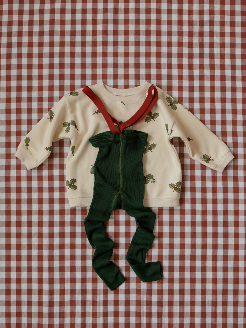 flat lay of organic toddler cream holly & candy cane sweatshirt with forest green tights with red braces