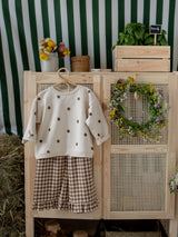 set of toddler brown checkered culottes with frill hems & cream sweatshirt with dots hanging on cupboard