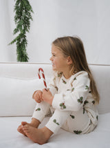 toddler in cream organic jersey pyjamas with holly & candy cane prints hugging knees holding candy cane