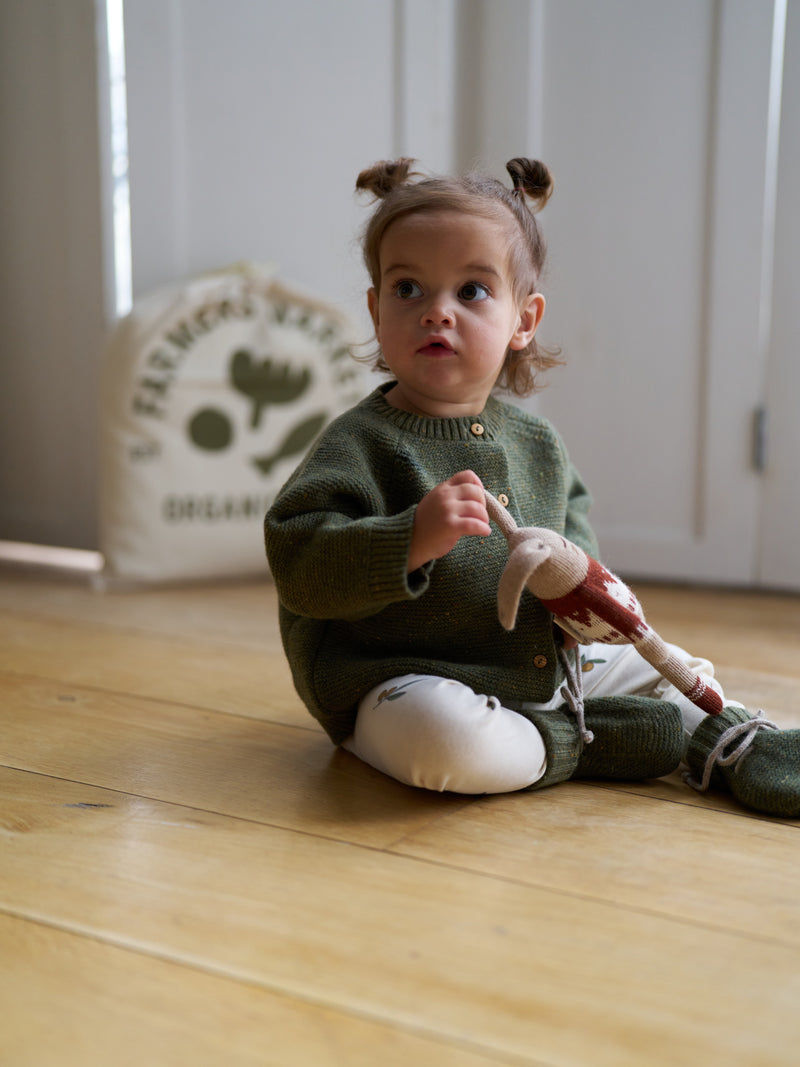 toddler dressed in organic forest green wool cardigan & booties with cream leggings holding wool toy