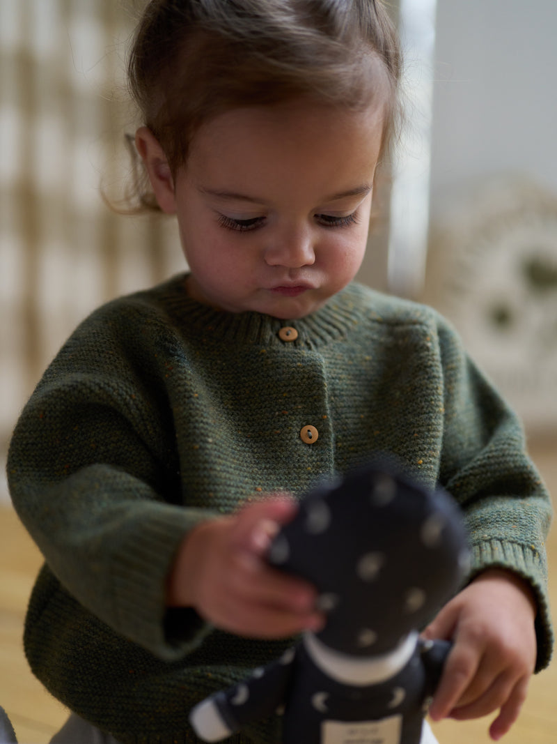 close up of toddler in forest moss green wool cardigan with wood buttons holding soft toy