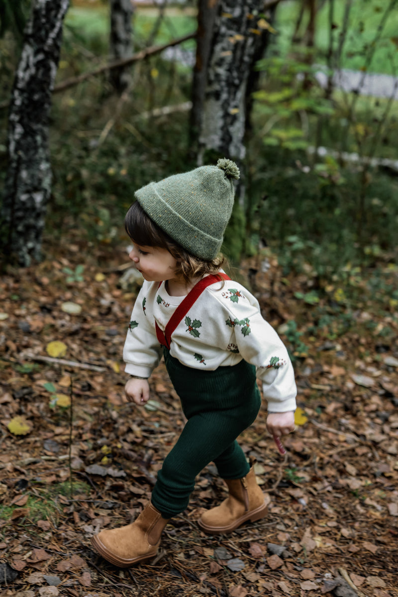 toddler in christmas holly & candy cane sweatshirt with green tights with braces beanie in forest 