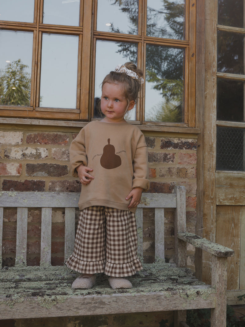 toddler in brown sweatshirt with pear print & gingham flannel culottes with frill hems & bun updo