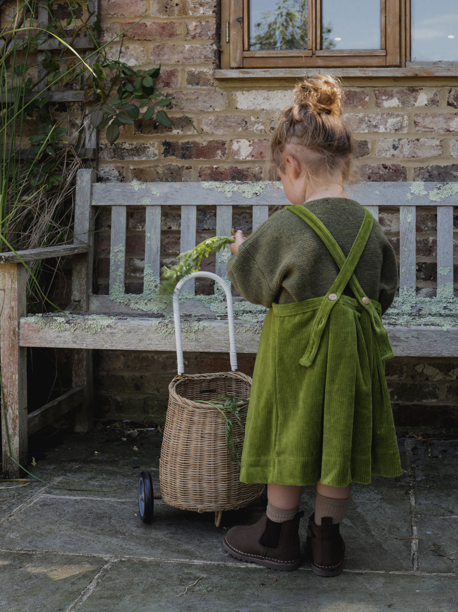 toddler wearing corduroy pinafore skirt in green with adjustable straps & sweatshirt with boots & bun updo