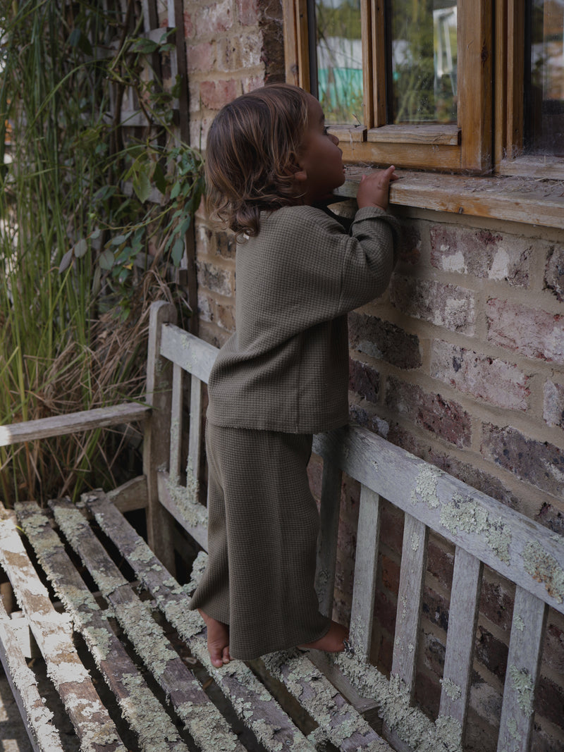 toddler in cotton waffle olive sweatshirt & long pants in tiptoes looking through windows