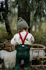 back view of toddler in holly & candy cane cream sweatshirt with forest green & red braces beanie in forest