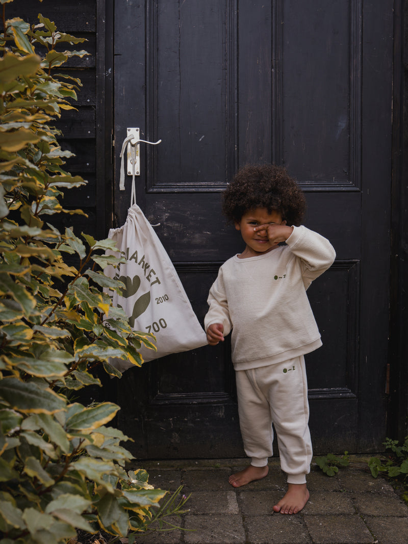 toddler in cream sweatshirt & sweatpants with embroidered text standing barefoot in front of door