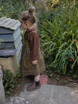 toddler wearing yellow & navy gingham flannel skirt & wool cardigan & boots with bun updo in garden