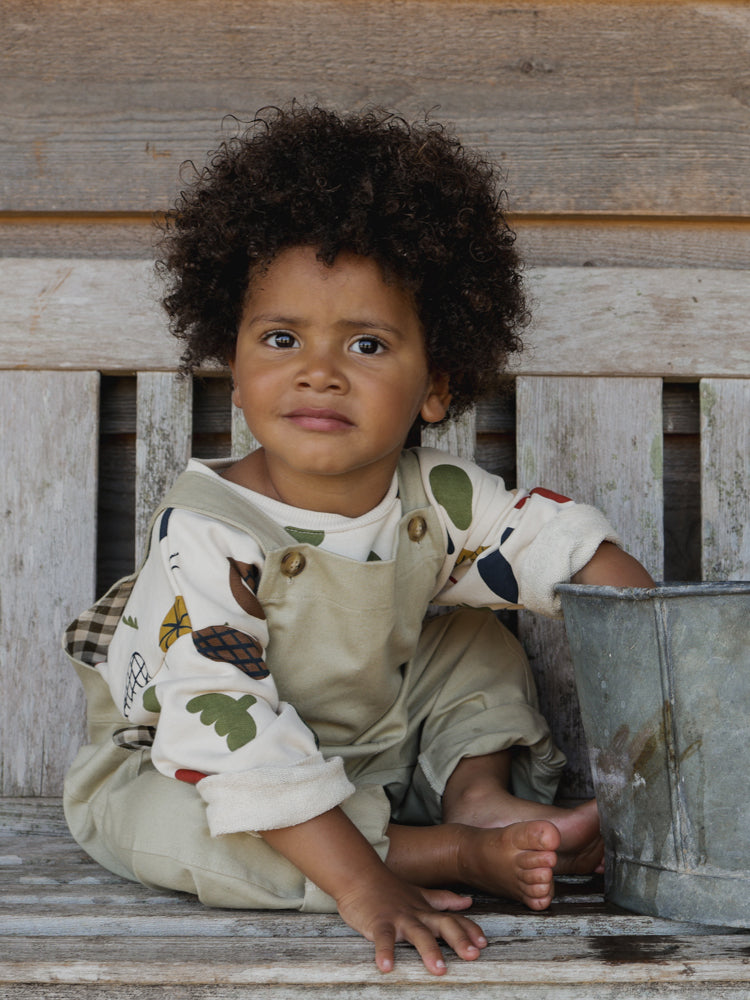 toddler in grey dungarees and sweatshirt with prints sitting on bench hand reaching inside bucket