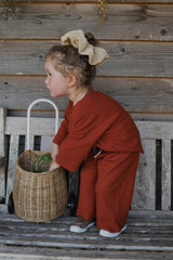 toddler dressed in matching red long pants & sweatshirt set with big scrunchie holding onto wicker trolley