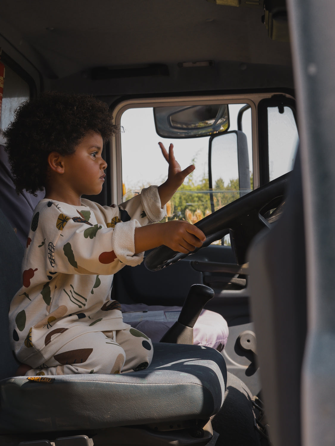 toddler in matching sweatshirt & sweatpants with farmers market produce print sitting in truck driver's seat