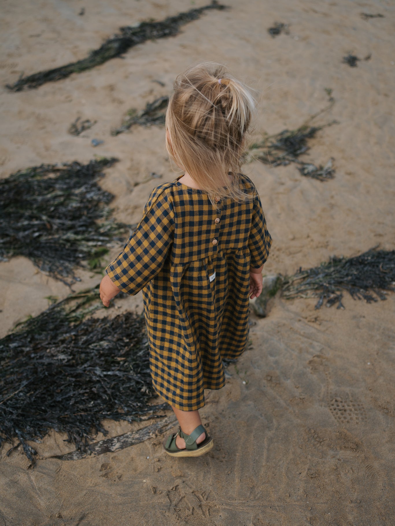 toddler in gingham dress with buttons on the back
