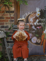 toddler in red wide leg pants & oversized sweatshirt at farmers market holding bread