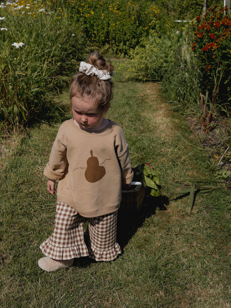 toddler in brown checkered frill hems culottes & brown sweatshirt pulling trolley with vegetables in farm