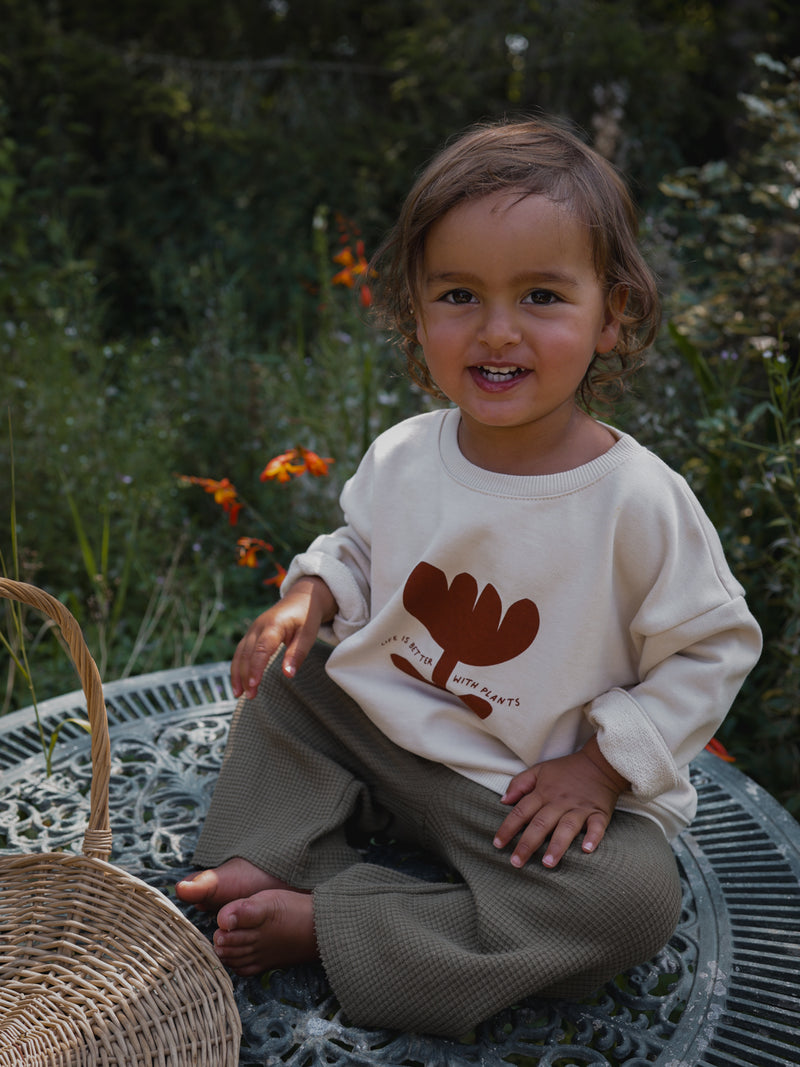 toddler in sweatshirt with print & text & waffle pants sitting on patio table in garden