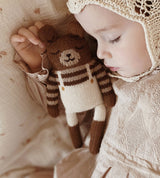 toddler sleeping while holding teddy knitted wool cuddly toy in stripes sweater & ecru overalls