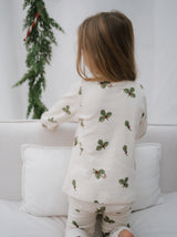 back view of toddler in matching organic jersey cream pyjamas with holly & candy cane kneeling on sofa