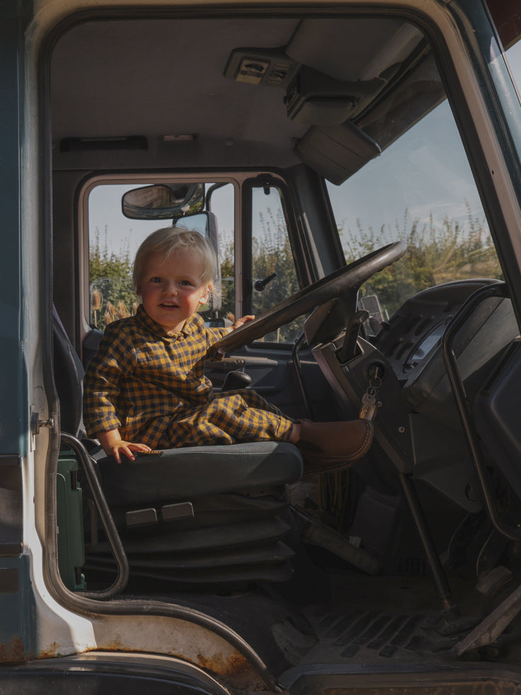 toddler in navy & yellow flannel shirt & pants set in a truck sitting in the driver's seat