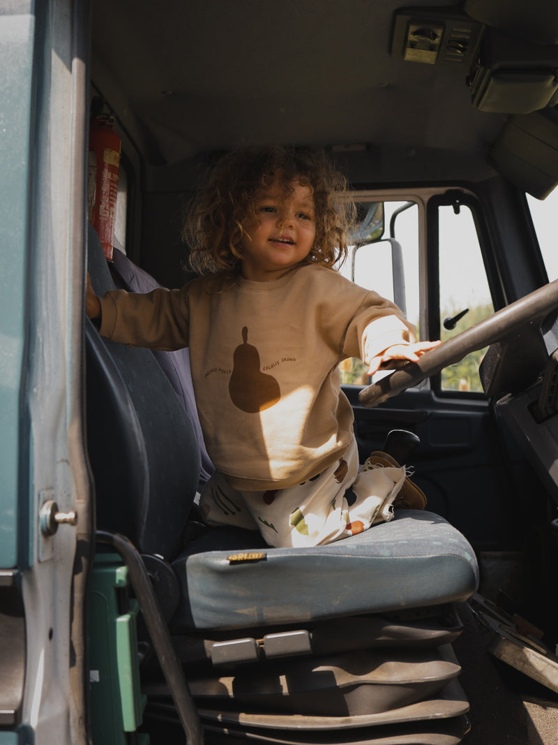 toddler in terry cotton sweatshirt with pear & cream long pants fiddling with truck steering wheel