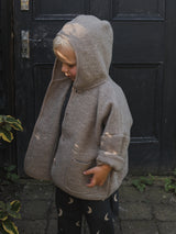 toddler wearing cream wool jacket with hood over head & black sweatpants with moon print