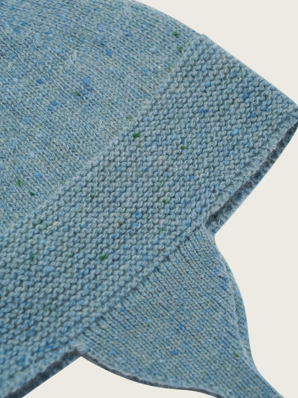 Close-up of a knitted textile item in a heathered light blue color with small green and darker blue flecks, showing the knit texture and folded edges against a white background.