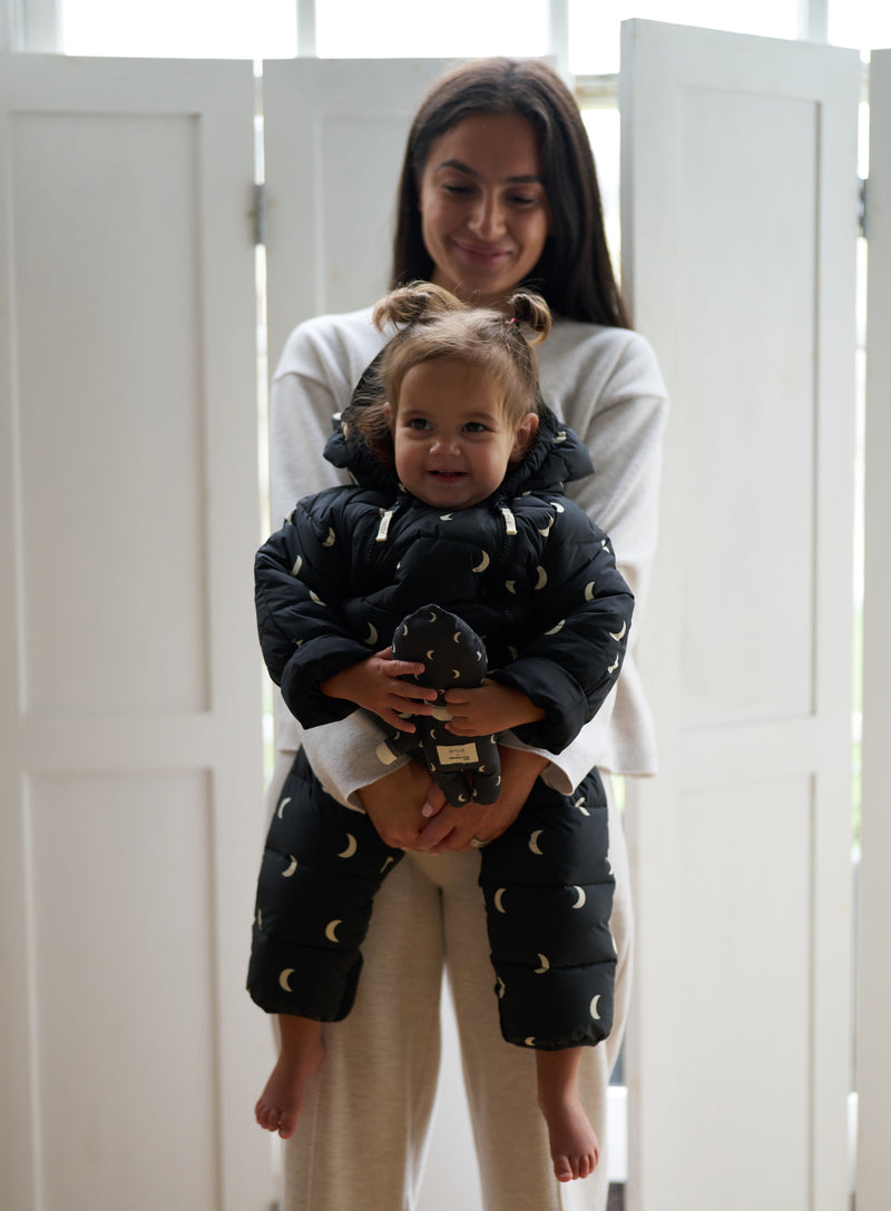 woman carrying baby padded snowsuit with white moons & hood holding soft toy with moon print