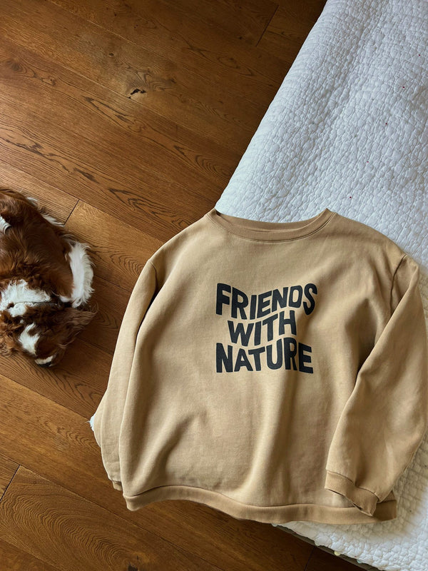 flat lay of women's brown sweater with FRIENDS WITH NATURE in wavy text across the front on bed